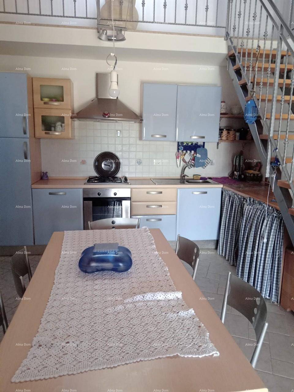 Funktionale Küche mit hellblauen Schränken, Esstisch und Treppe zum oberen Bereich.