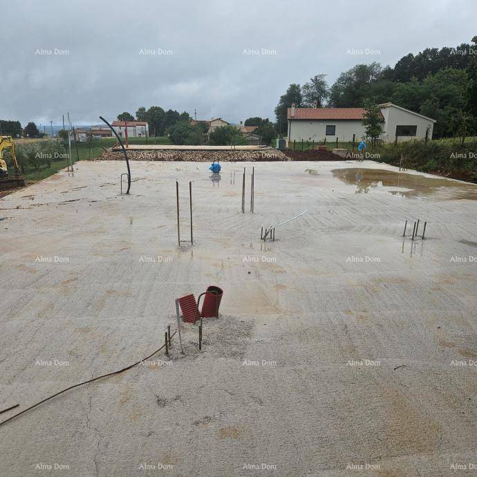 Weitläufige Betonfundamentplatte einer Baustelle mit sichtbaren Rohren und Bewehrungsstäben, umgeben von Häusern.