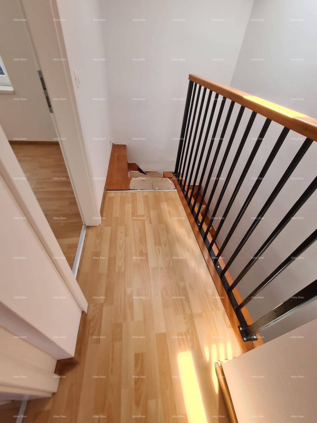 Heller Flur mit Laminatboden und einer Holztreppe mit schwarzen Metallgeländern.
