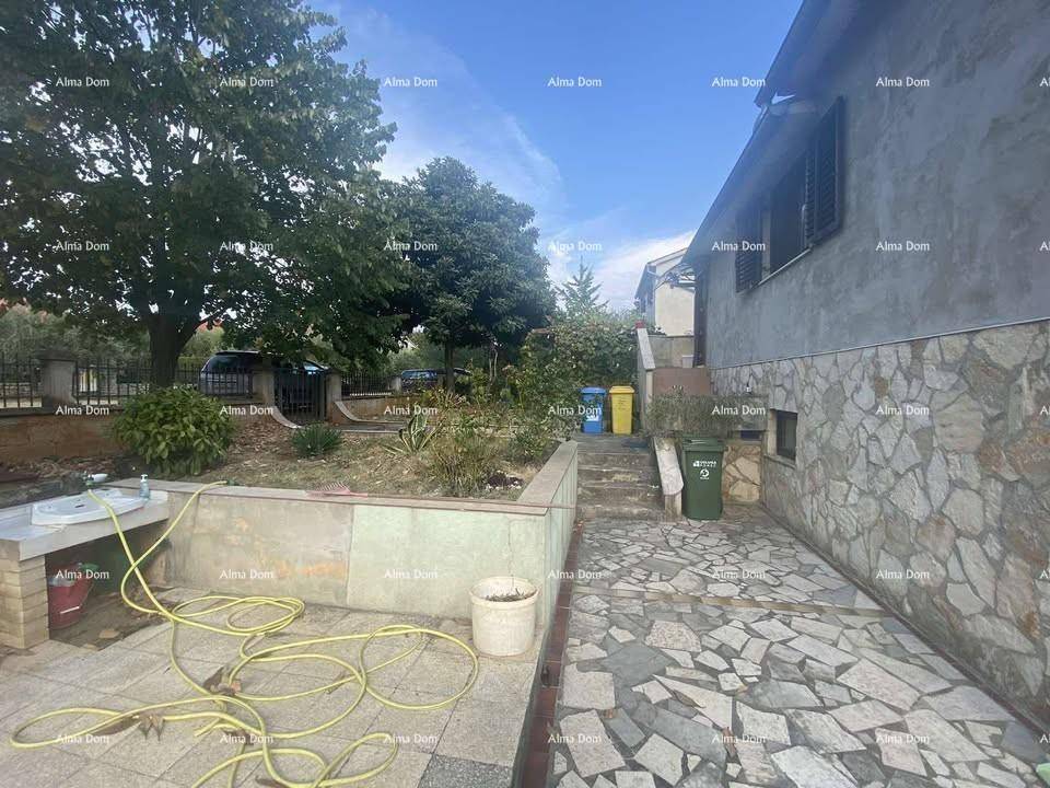 Hausfassade mit Steindetails, gepflastertem Bereich mit Außenwaschbecken und Garten.