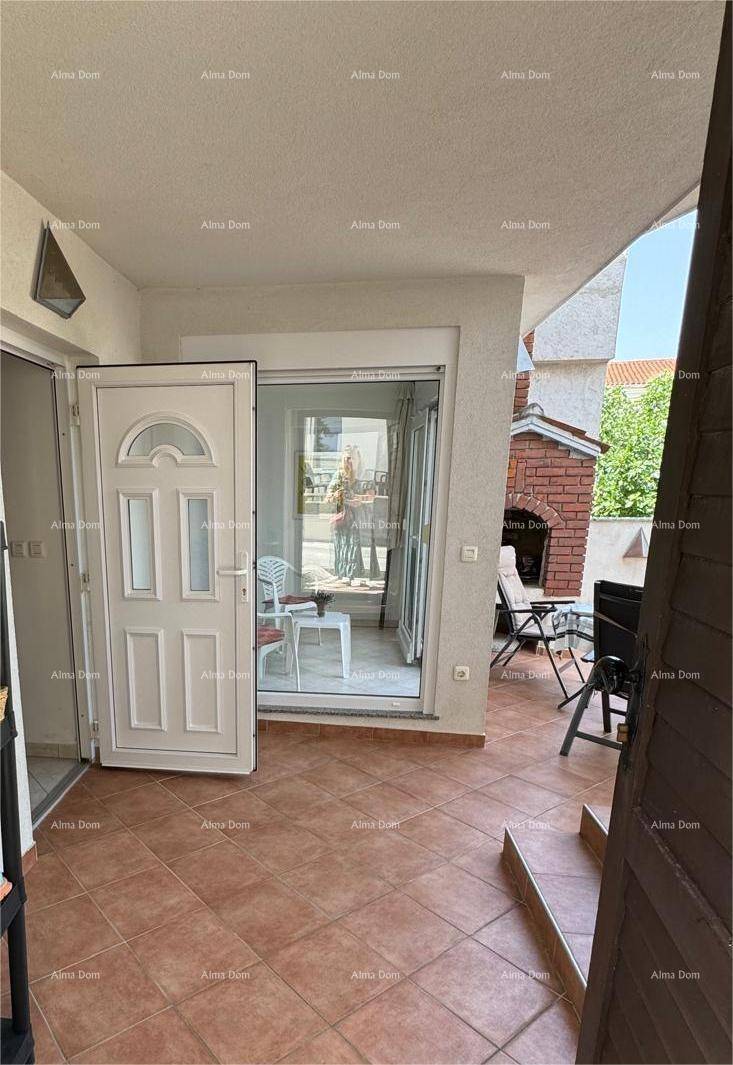 Überdachter Terrassenbereich mit Zugang zum Haus und einem gemauerten Grill im Hintergrund.
