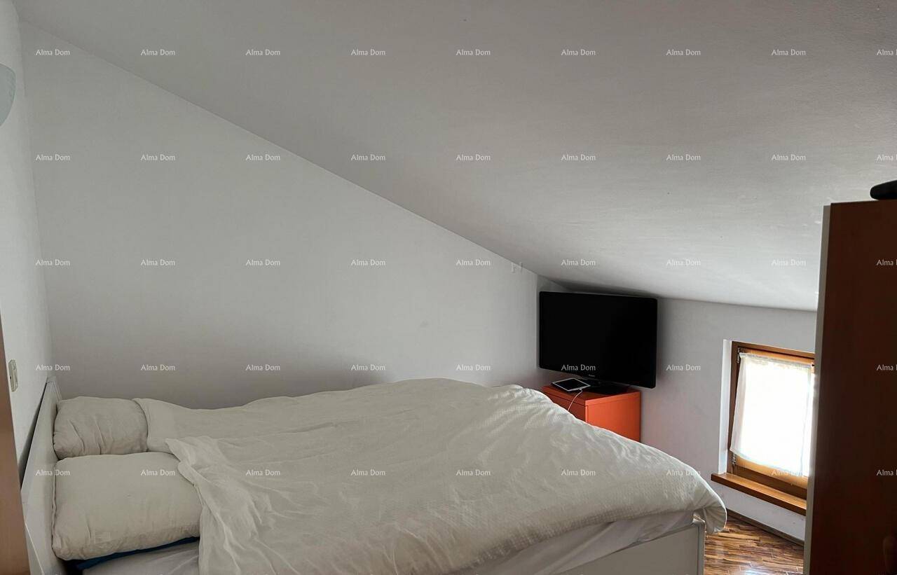 Helles Schlafzimmer im Dachgeschoss mit schrägen Wänden, einem großen Bett und einem Fernseher.