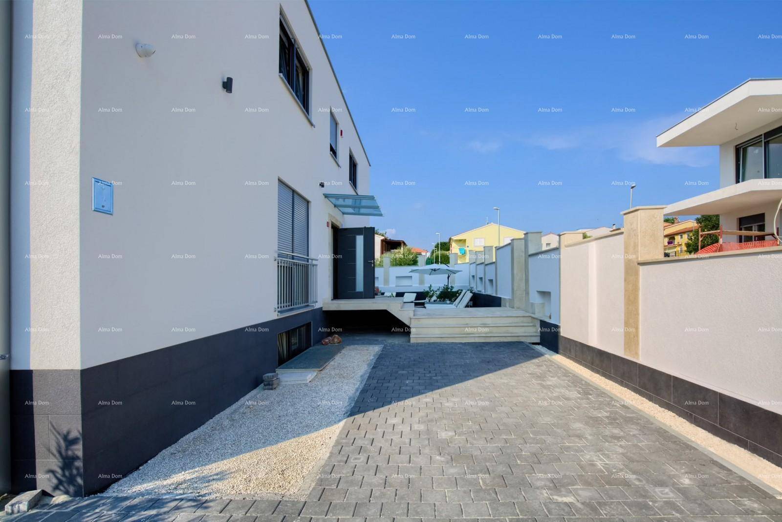 Seitenansicht eines modernen Hauses mit gepflasterter Zufahrt und angrenzenden Mauern unter klarem Himmel.