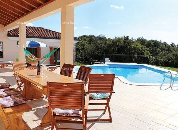Überdachte Terrasse mit großem Esstisch und Stühlen, direkt am Pool mit Blick ins Grüne.