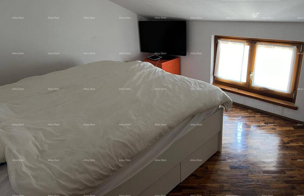 Schlafzimmer im Dachgeschoss mit Doppelbett, Holzboden und einem Fenster, das Tageslicht hereinlässt.