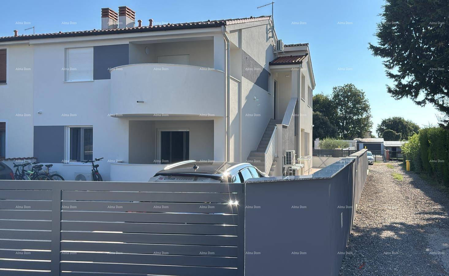 Moderne Wohngebäude-Fassade mit Balkonen, Zufahrt und einem geparkten Auto davor.