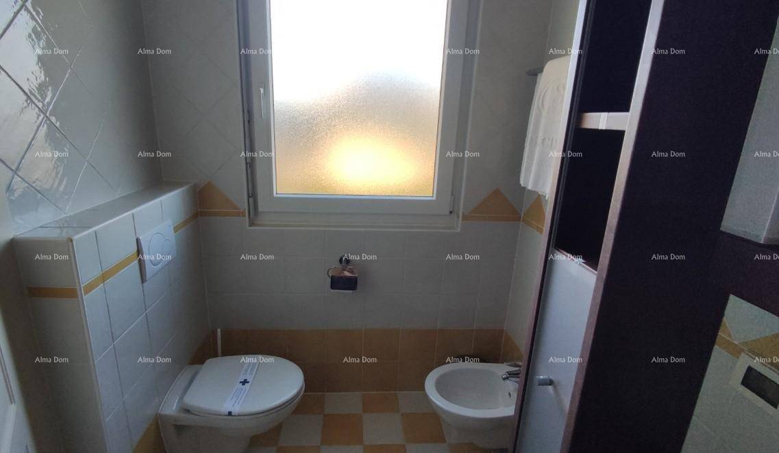Badezimmer mit WC, Bidet und Fenster, gestaltet mit gelb-weißen Fliesen und Ablageflächen.