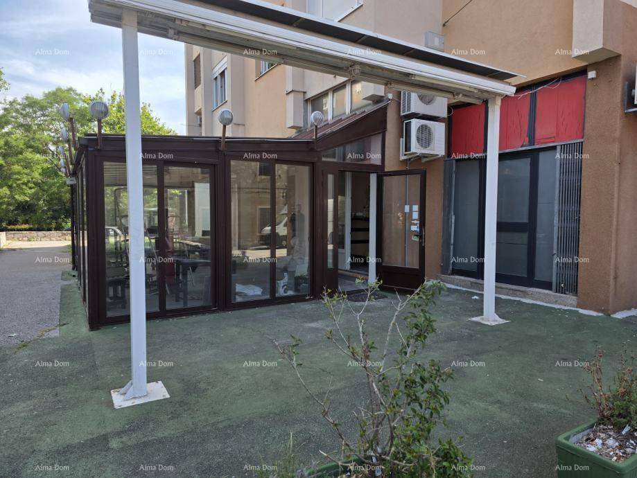 Außenansicht eines Gebäudes mit verglastem Anbau und künstlicher Rasenfläche davor.