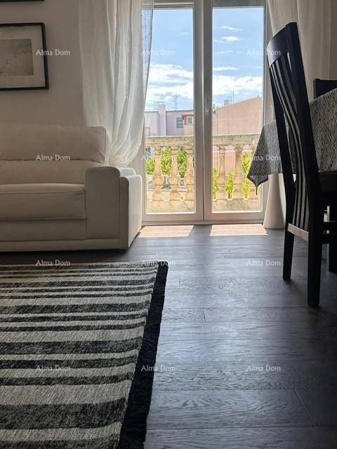 Heller Wohnbereich mit Zugang zu einem Balkon, dunklem Holzboden und einem gestreiften Teppich.