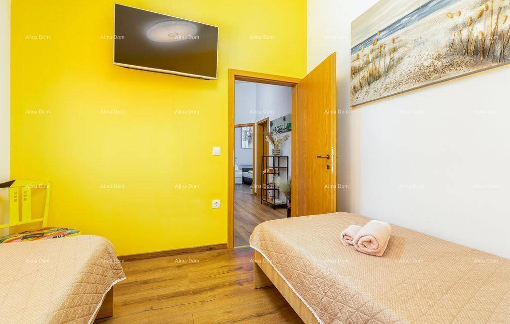 Helles Schlafzimmer mit zwei Einzelbetten, gelber Akzentwand und Holzboden, mit Blick in den Flur.