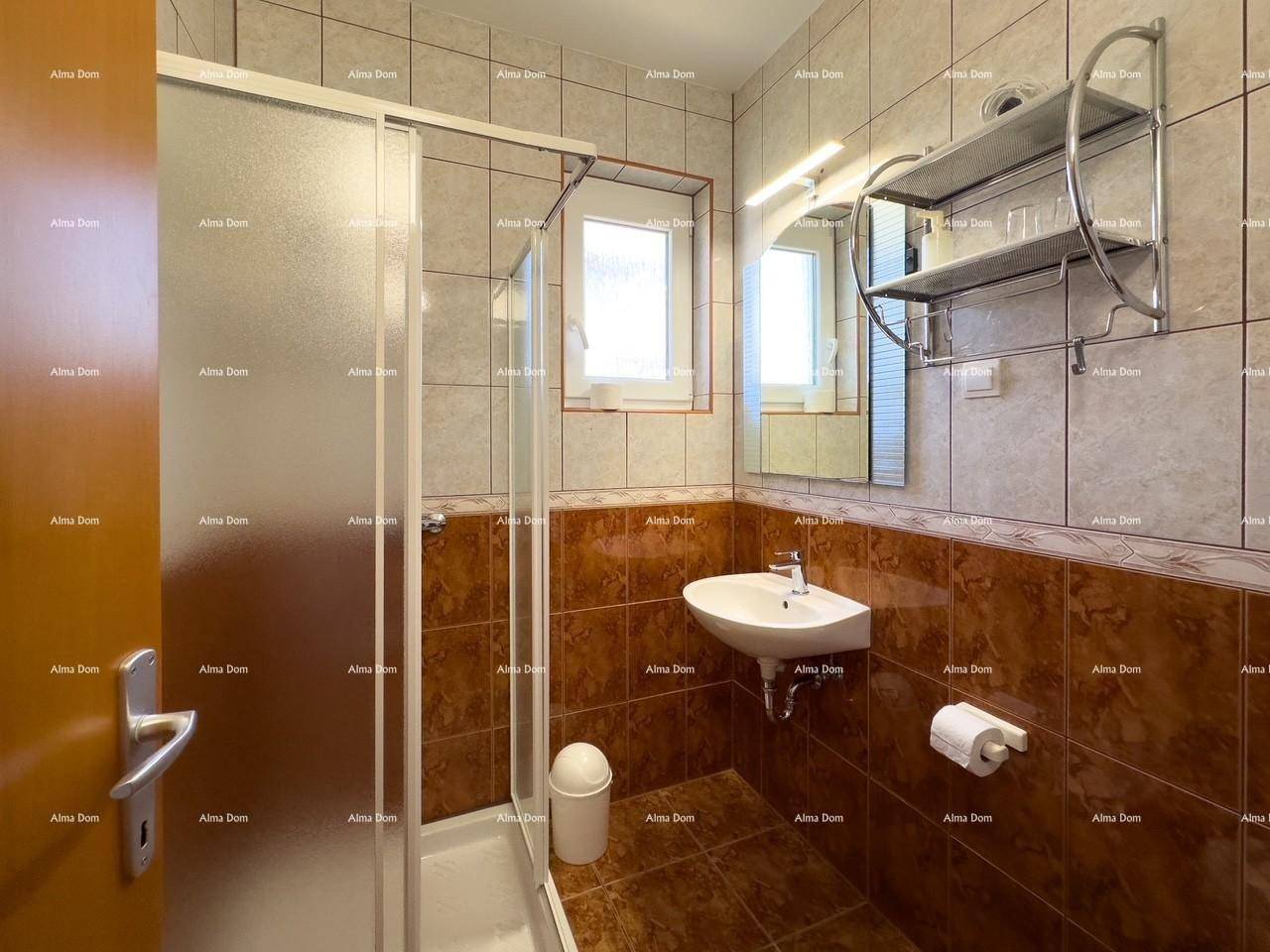 Gefliestes Badezimmer mit Duschkabine, kleinem Waschbecken und Fenster.