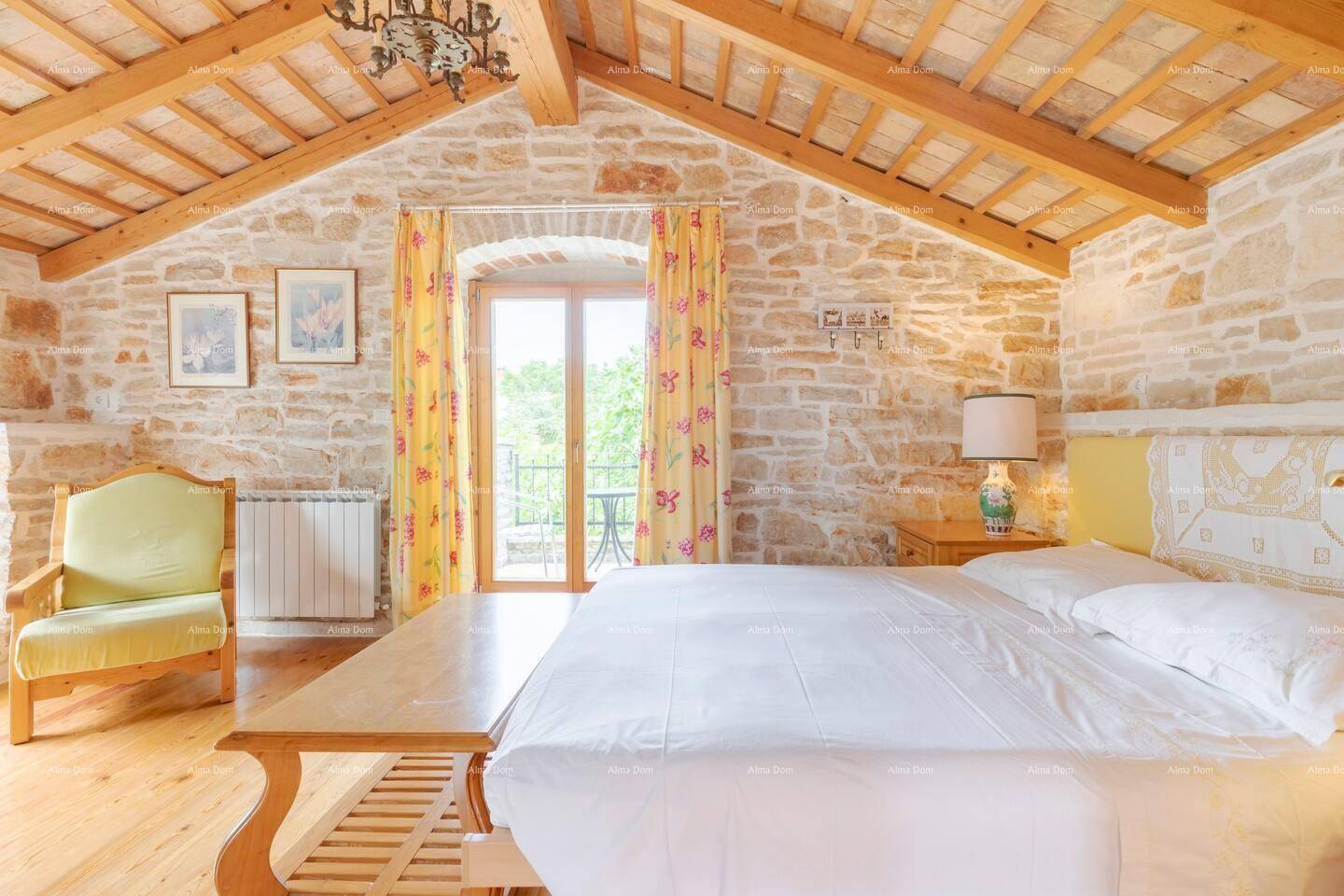 Schlafzimmer im Dachgeschoss mit Holzbalkendecke, Steinwänden und Zugang zu einem französischen Balkon.