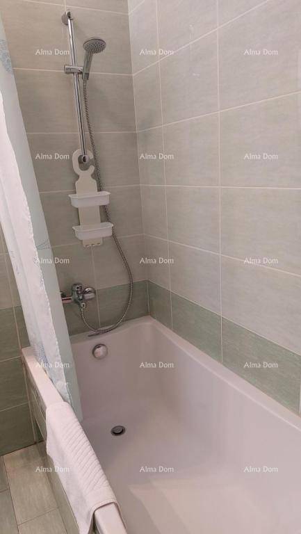 Badezimmer mit Badewanne und integrierter Duschfunktion, umgeben von hellgrünen Fliesen.