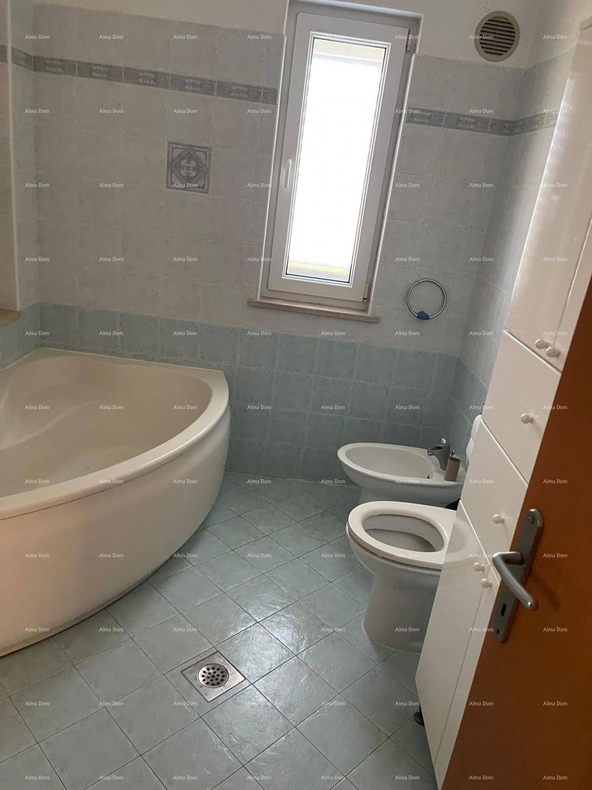 Badezimmer mit Eckbadewanne, Toilette, Bidet und einem Fenster, gefliest in Blau- und Weißtönen.