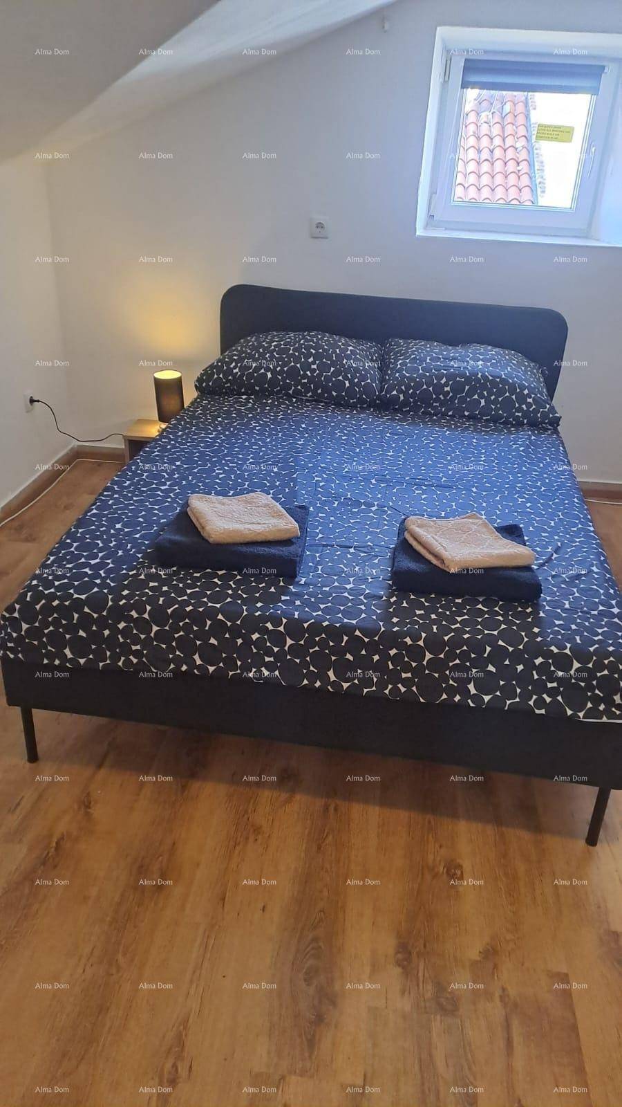 Schlafzimmer mit Doppelbett und kleinem Fenster im Dachgeschoss, mit dunkler Bettwäsche.