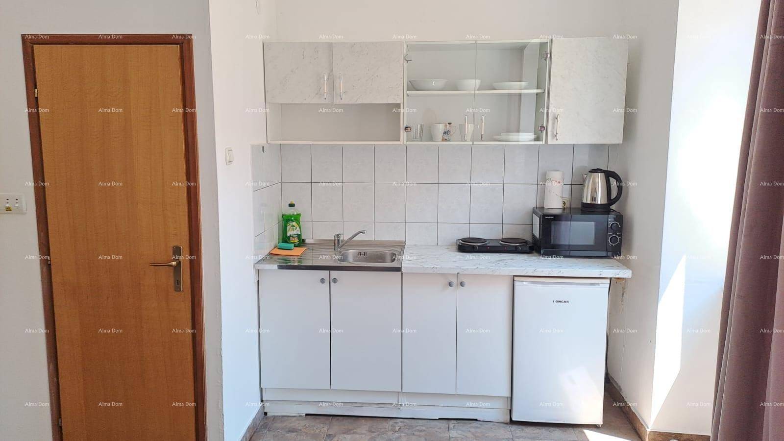Einfache weiße Küchenzeile mit Spüle, Kochplatten und Kühlschrank, ideal für ein kleines Apartment.