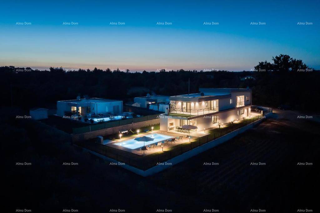 Beeindruckende Luftaufnahme der beleuchteten Villa mit Pool und umliegenden Gebäuden bei Nacht.