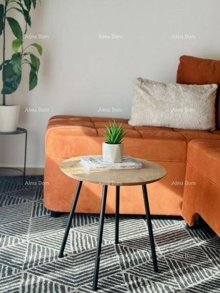 Detailaufnahme eines modernen Beistelltisches vor einem orangefarbenen Sofa mit Kissen.