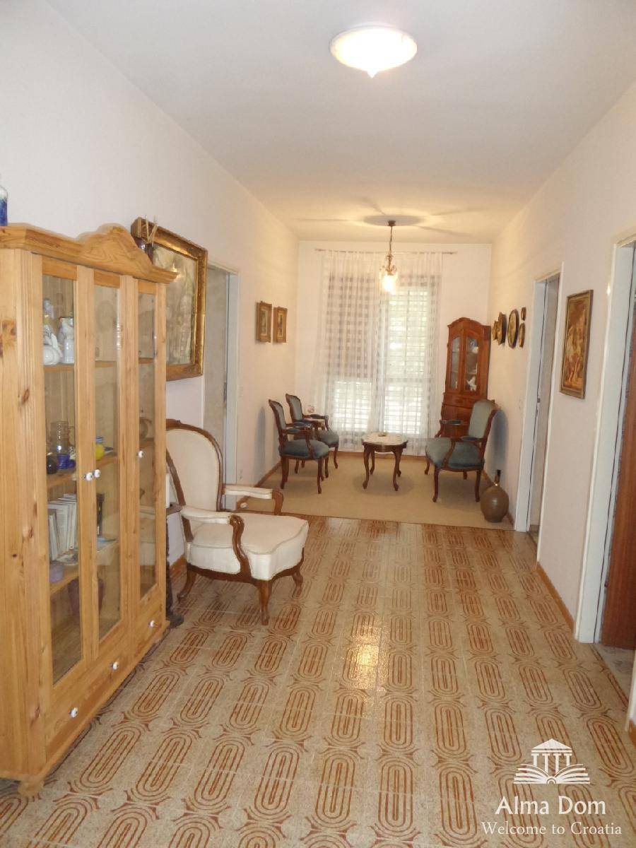 Langer Flur mit gemusterten Fliesen, Holzschrank und Blick in einen traditionell eingerichteten Wohnbereich.