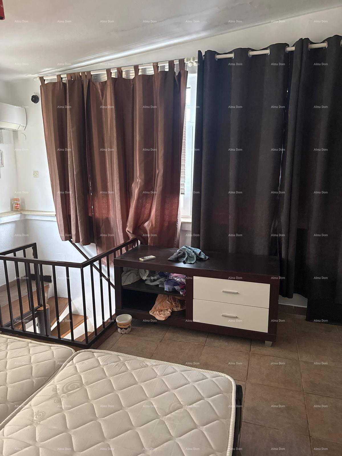 Schlafzimmer mit dunklen Vorhängen vor den Fenstern und einem Geländer, das den Blick nach unten freigibt.