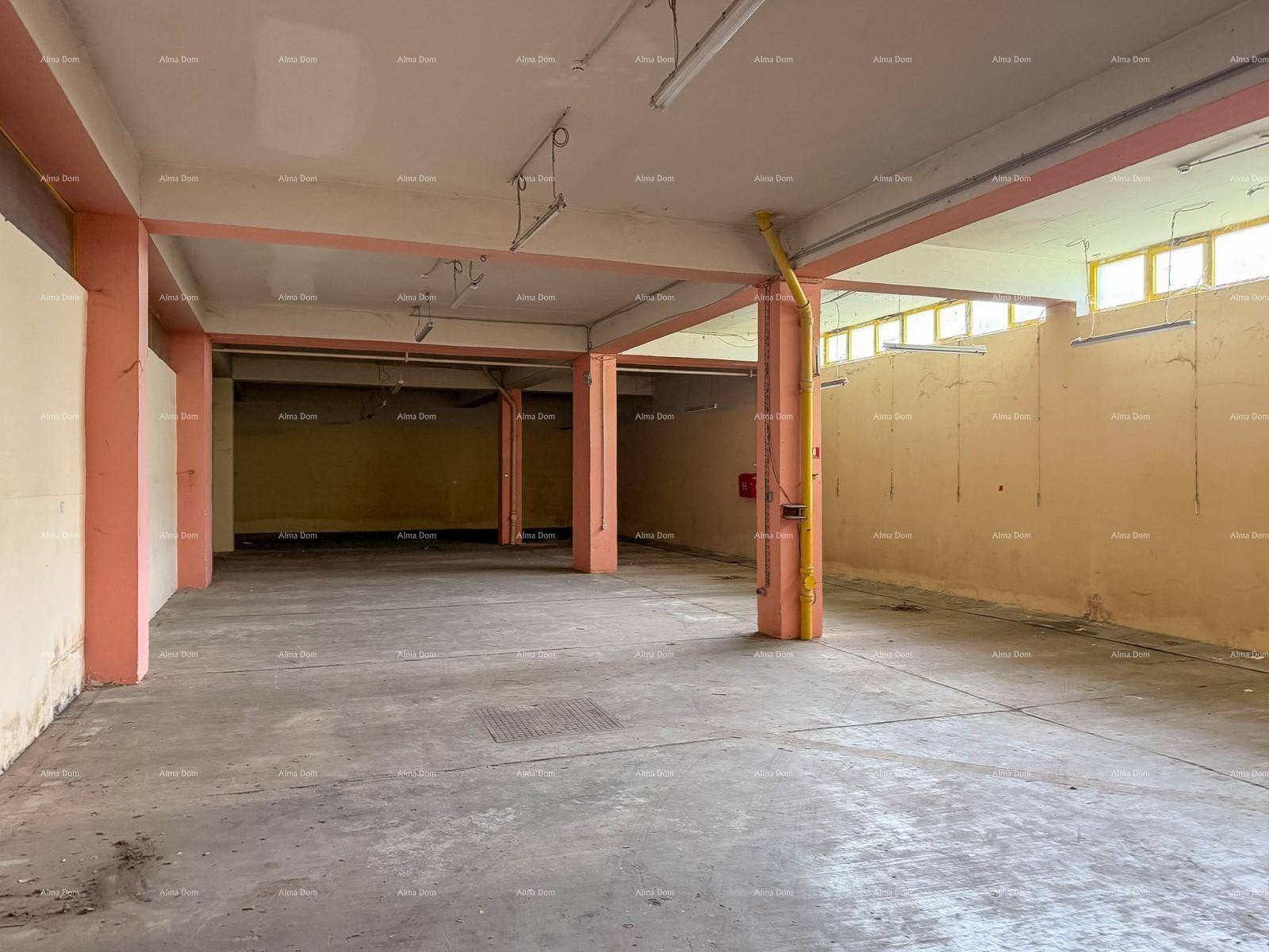 Weitläufiger, leerer Lagerraum mit Betonboden, rosa Stützpfeilern und gelben Leitungen unter der Decke.