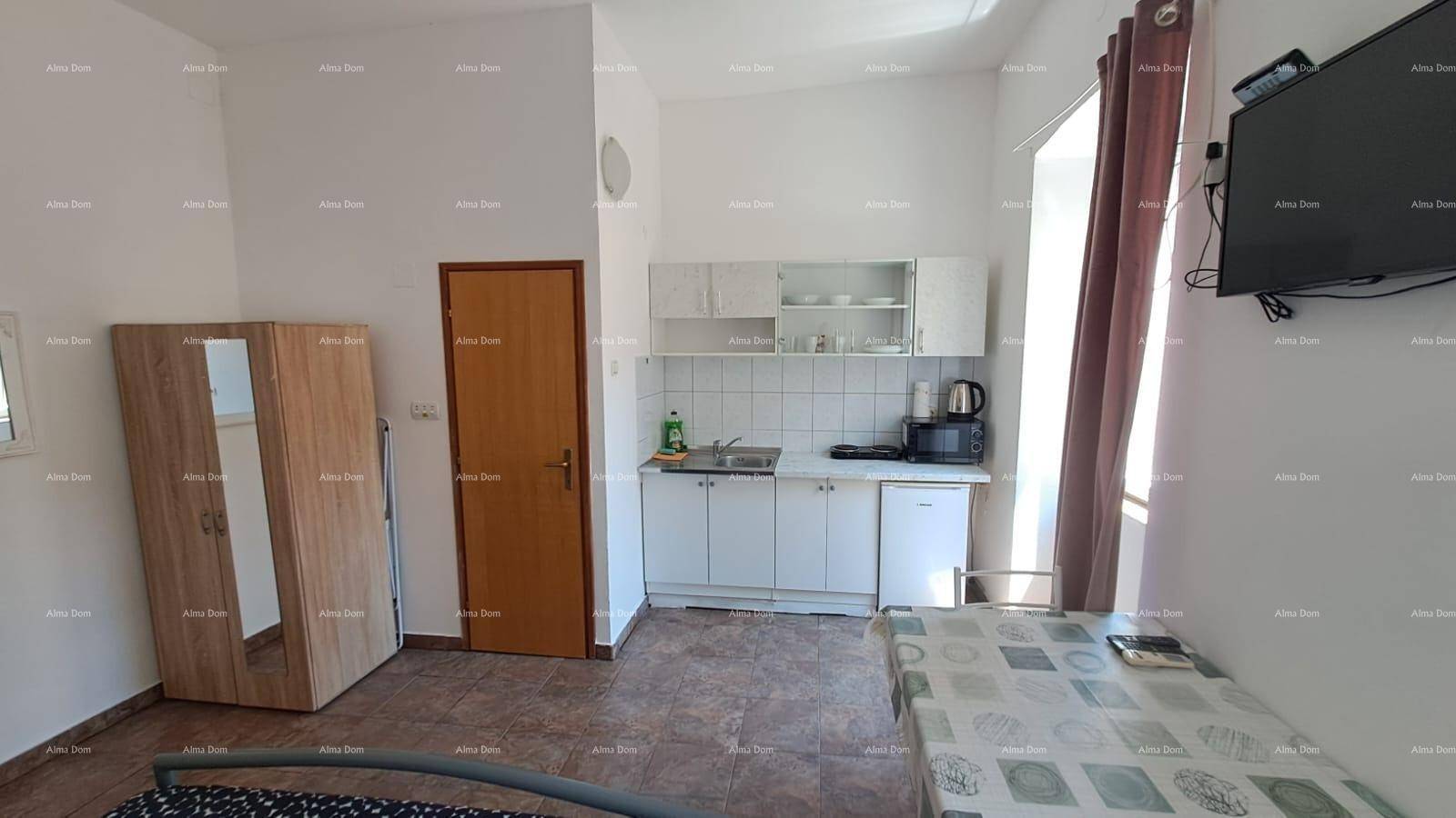 Studio-Apartment mit Schlafbereich, Esstisch und integrierter weißer Küchenzeile, funktional eingerichtet.