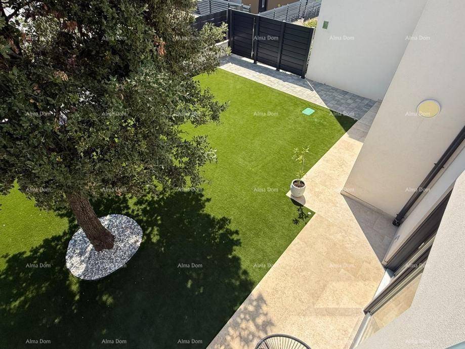Kleiner, gepflegter Gartenbereich mit Baum, Kunstrasen und Zugangstor, umgeben von einer Mauer.