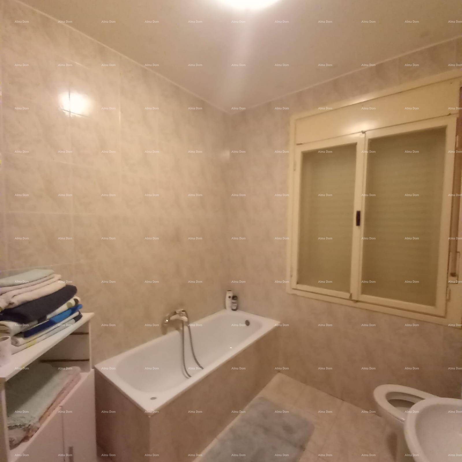 Badezimmer mit Badewanne, beigefarbenen Fliesen und einem Fenster für Tageslicht.