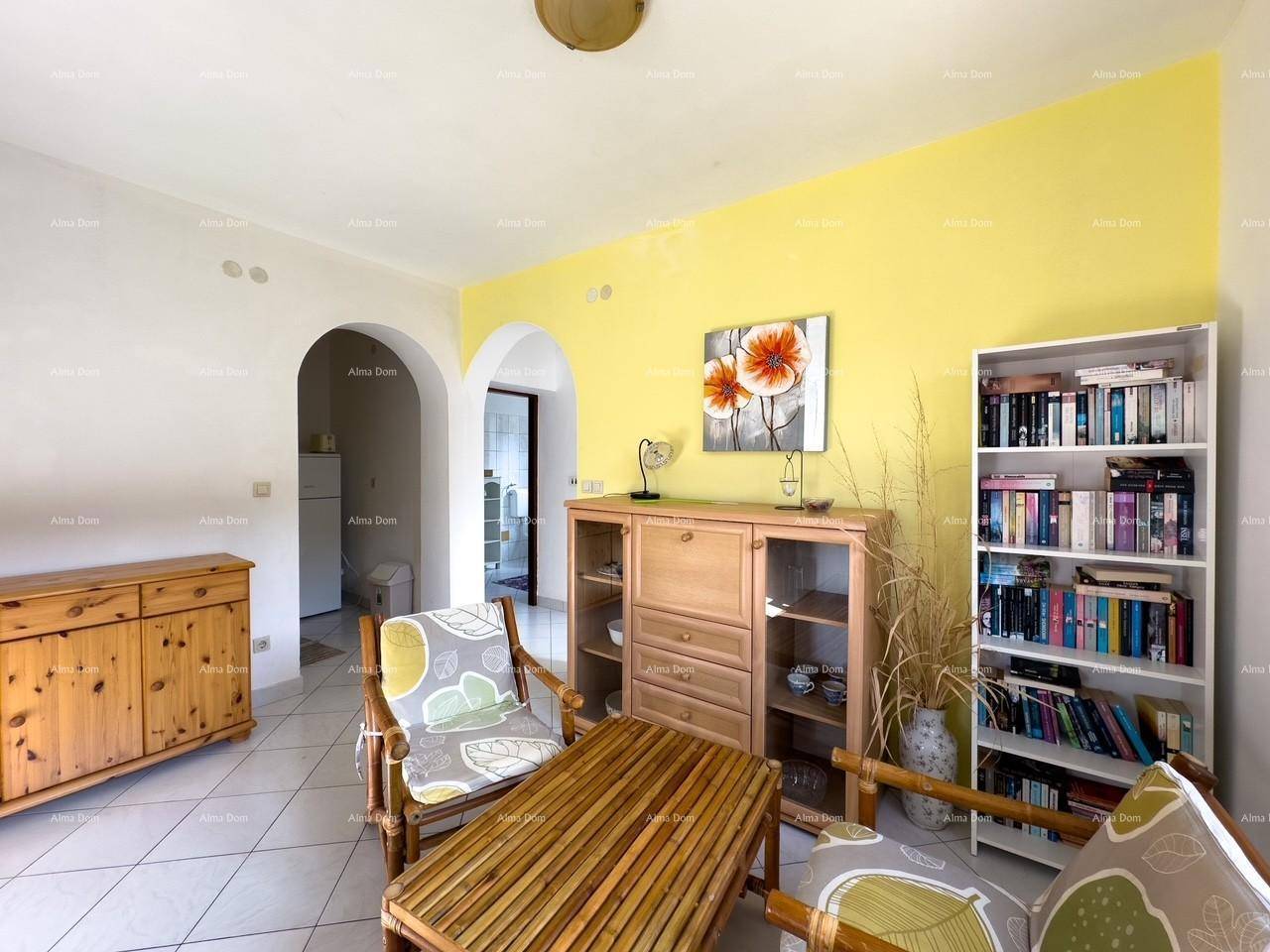 Detailansicht des Wohnzimmers mit gelber Wand, Holzmöbeln und einem Bücherregal, durch Bögen verbunden.