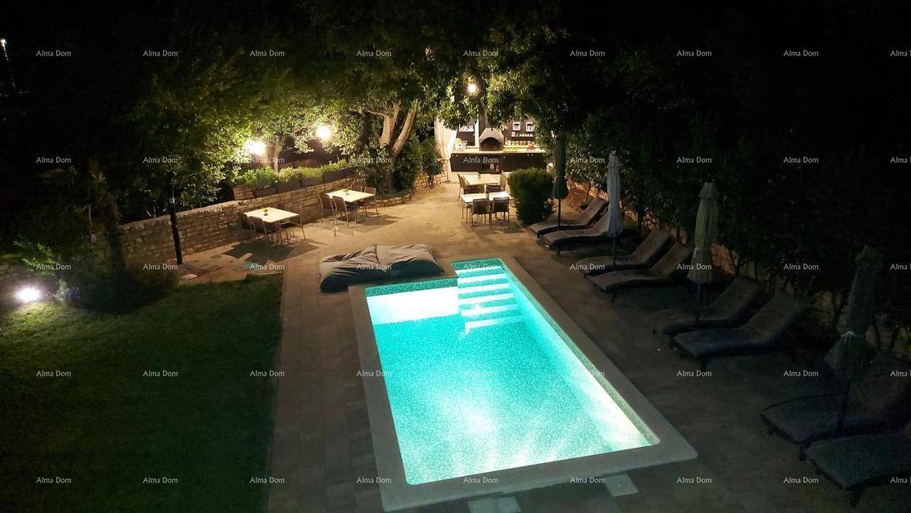 Beleuchteter Gartenbereich bei Nacht mit Pool, Liegestühlen und einer gemütlichen Außenküche.