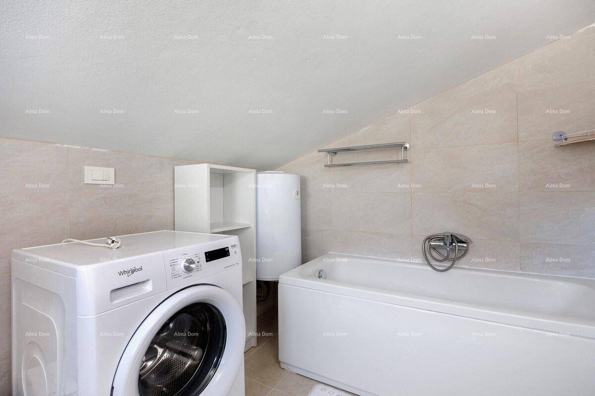 Badezimmer mit Badewanne, Waschmaschine und Warmwasserbereiter, unter einem Schrägdach.