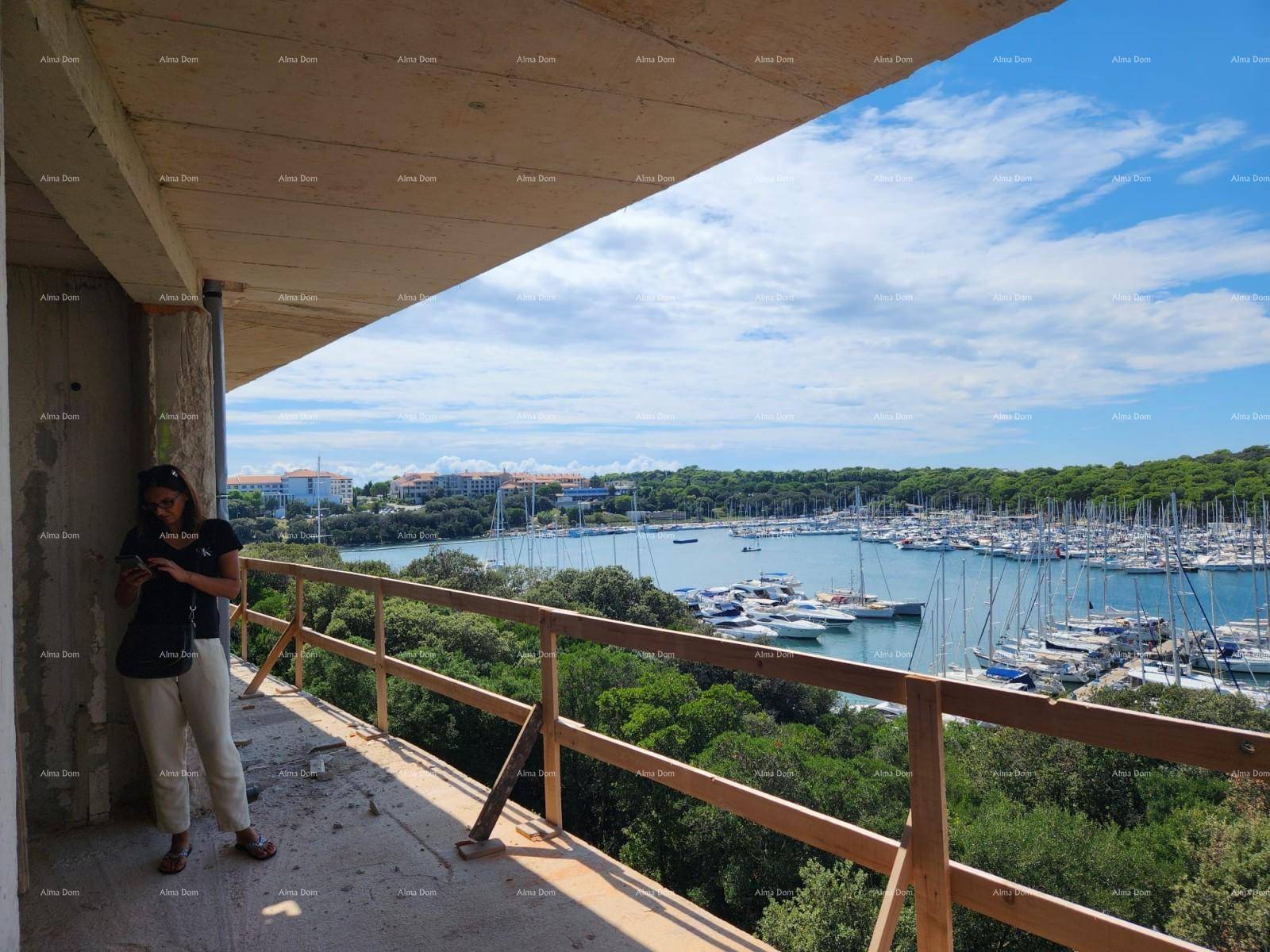 Person auf einem unfertigen Balkon genießt den weiten Blick auf den Yachthafen und die grüne Küste.