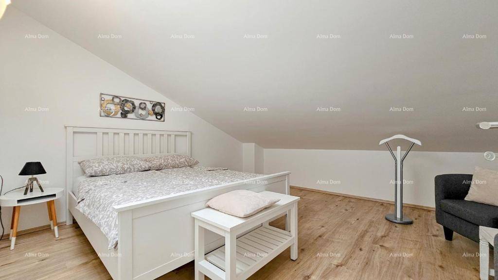 Geräumiges Schlafzimmer im Dachgeschoss mit Holzboden, weißem Bett und Sitzgelegenheit.