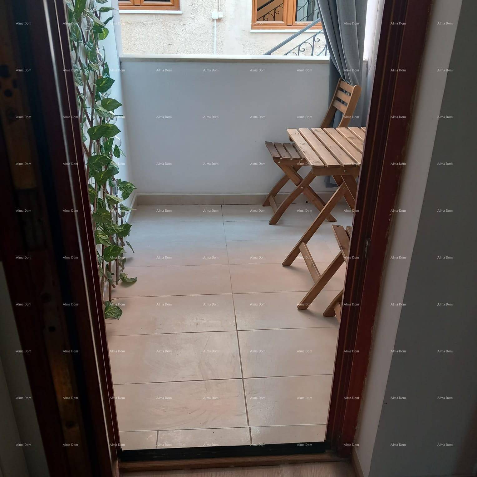 Kleiner, gefliester Balkon mit Holztisch und Stühlen, umgeben von einer Rankpflanze.