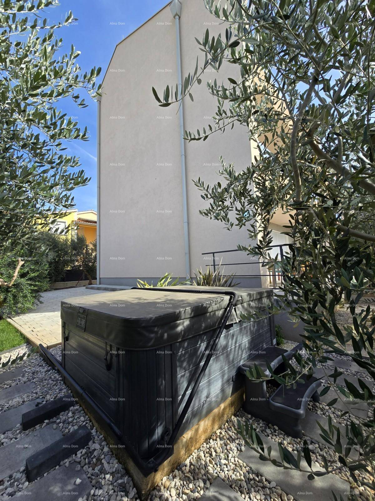 Moderne Gebäudefassade mit einem Whirlpool im Vorgarten, umgeben von mediterraner Bepflanzung.