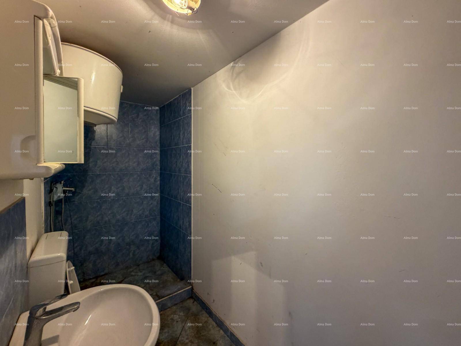 Kleines Badezimmer mit blauen Fliesen im Duschbereich, Toilette, Waschbecken und Warmwasserboiler.