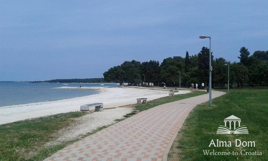 Gepflasterter Weg entlang eines Sandstrandes mit Bäumen und Meerblick, ideal für Spaziergänge.