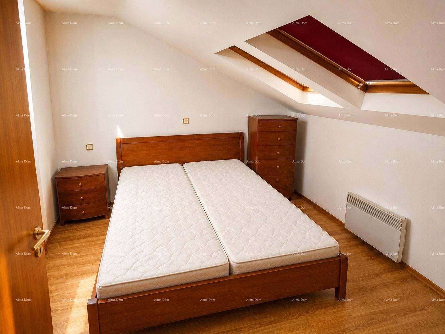 Helles Schlafzimmer im Dachgeschoss mit Doppelbett, Heizkörper und großem Dachfenster.