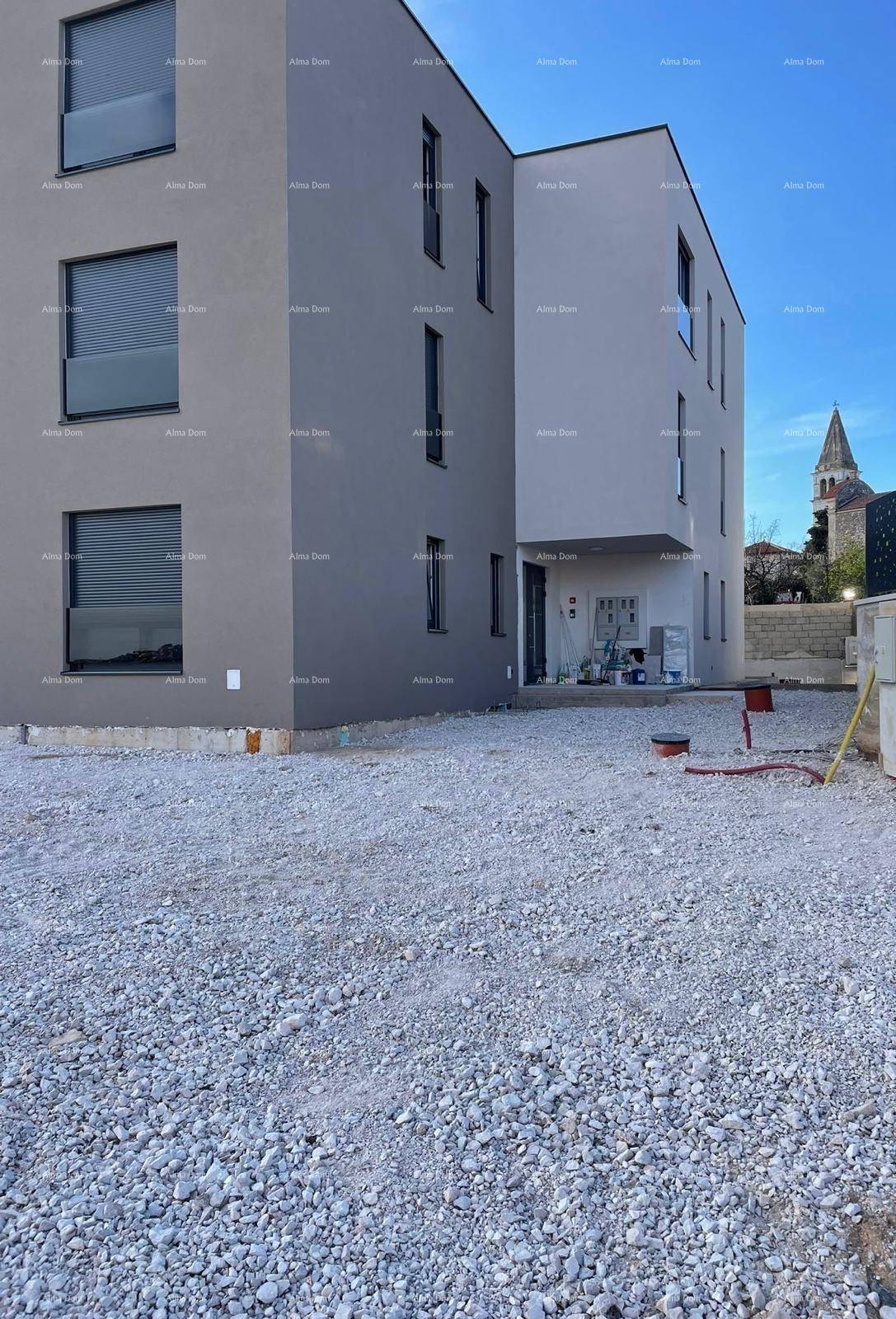 Moderne Gebäudefassade eines Neubaus mit klaren Linien und einem Kirchturm im Hintergrund.