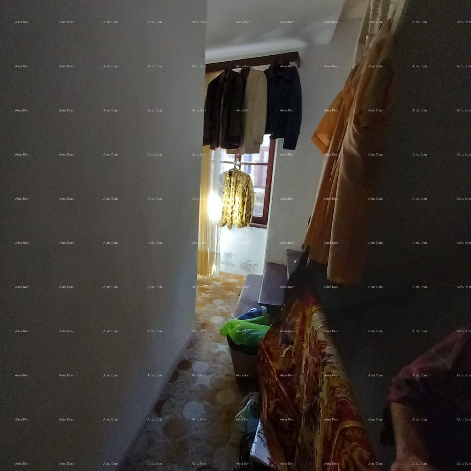 Schmaler Flur mit Kleidern an der Wand und einem Fenster am Ende des Ganges.