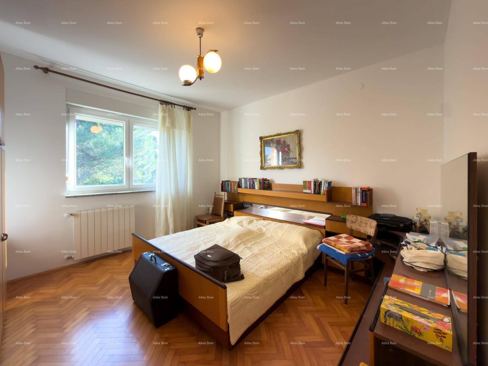 Schlafzimmer mit Doppelbett, Parkettboden, großem Fenster und Bücherregal am Kopfteil.