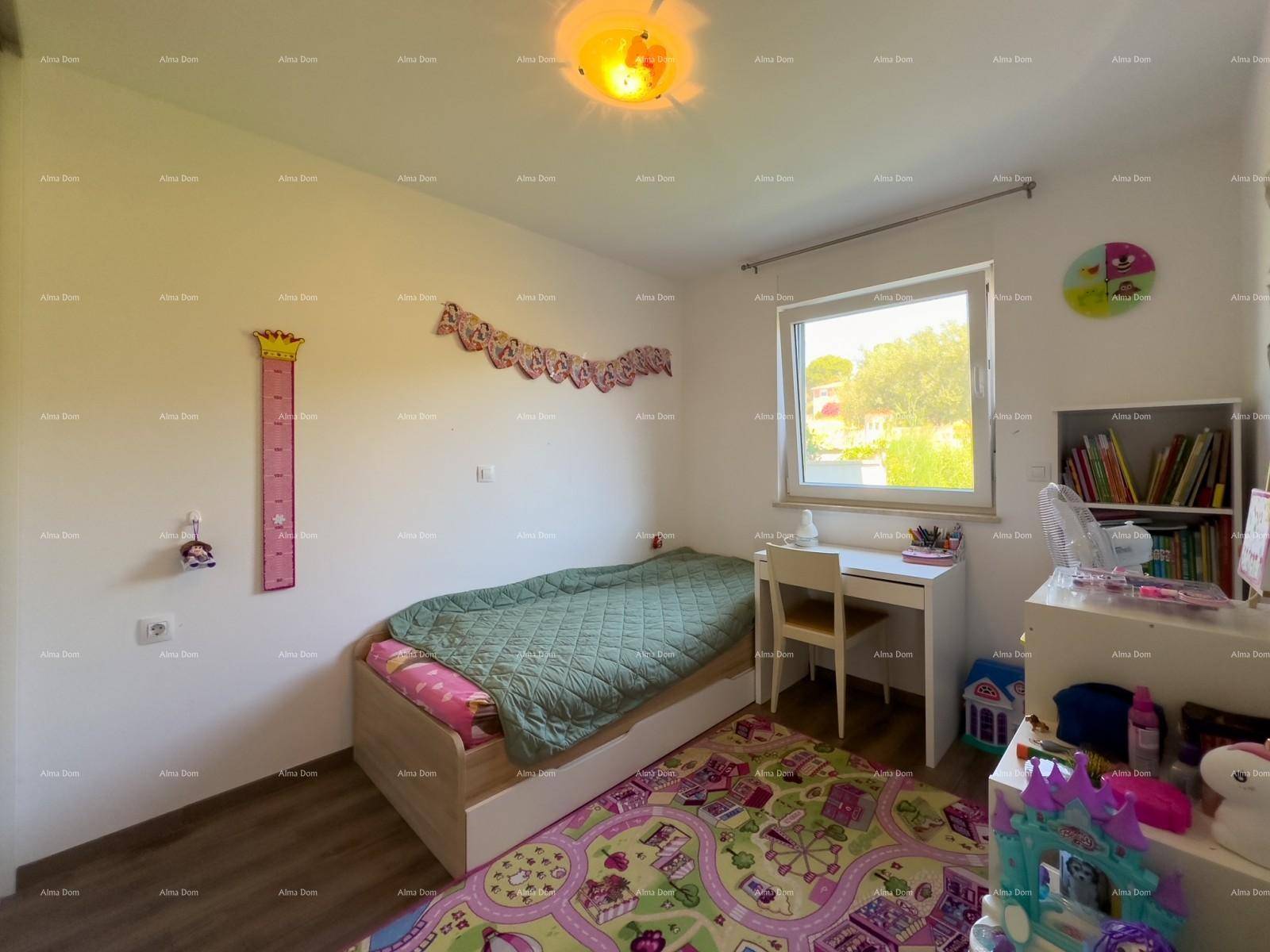Kinderzimmer mit Einzelbett, Schreibtisch und farbenfrohem Teppich, mit Blick ins Grüne.