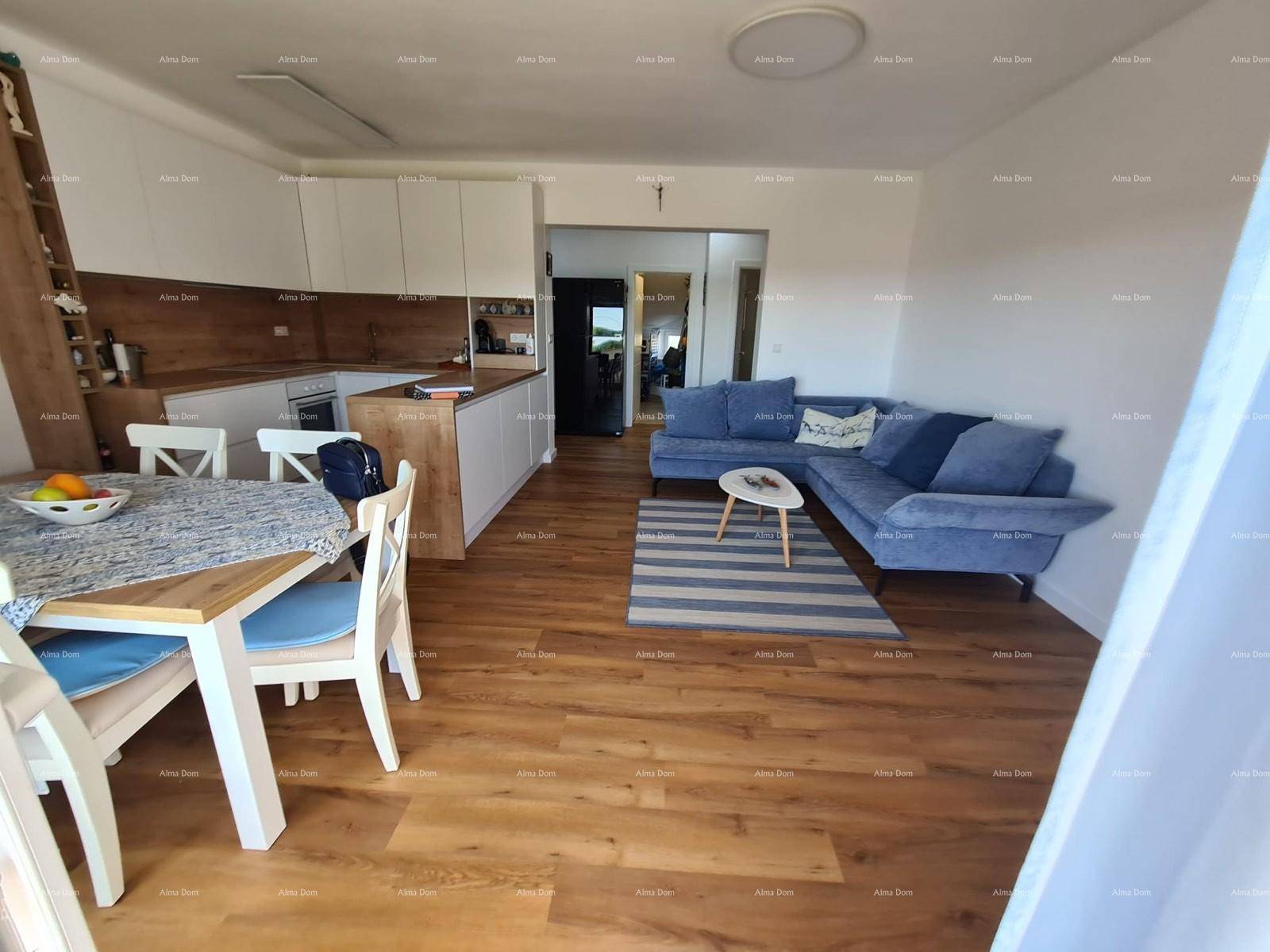 Offener Wohnbereich mit integrierter Küche, Essplatz und gemütlichem Sofa, alles auf hellem Holzboden.