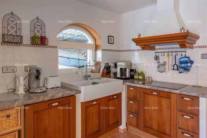 Traditionelle Küche mit Holzschränken, Bauernspüle, Stein-Arbeitsplatten und gewölbtem Fenster.