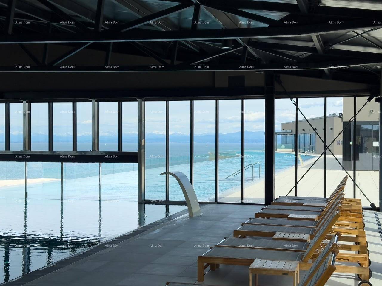 Innenpoolbereich mit Liegestühlen und großen Fenstern, die den Blick auf den Außenpool und das Meer freigeben.