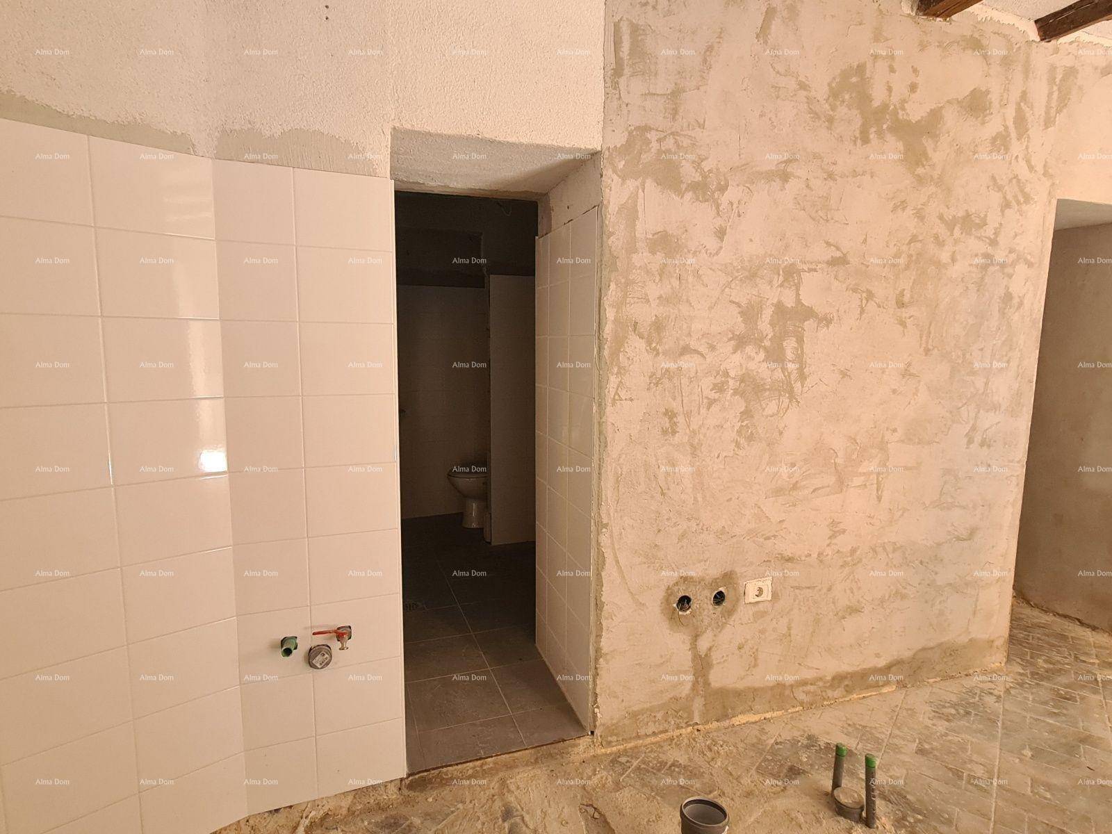 Innenraum im Rohbau mit teilweise gefliesten Wänden und Blick auf ein Badezimmer.