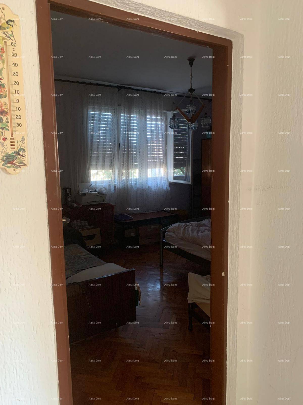 Blick durch eine Tür in ein Schlafzimmer mit zwei Betten, Parkettboden und Fenstern mit Jalousien.