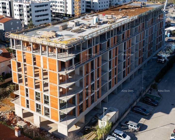 Seitenansicht des im Bau befindlichen Gebäudes mit sichtbaren Etagen und umliegenden Parkplätzen.