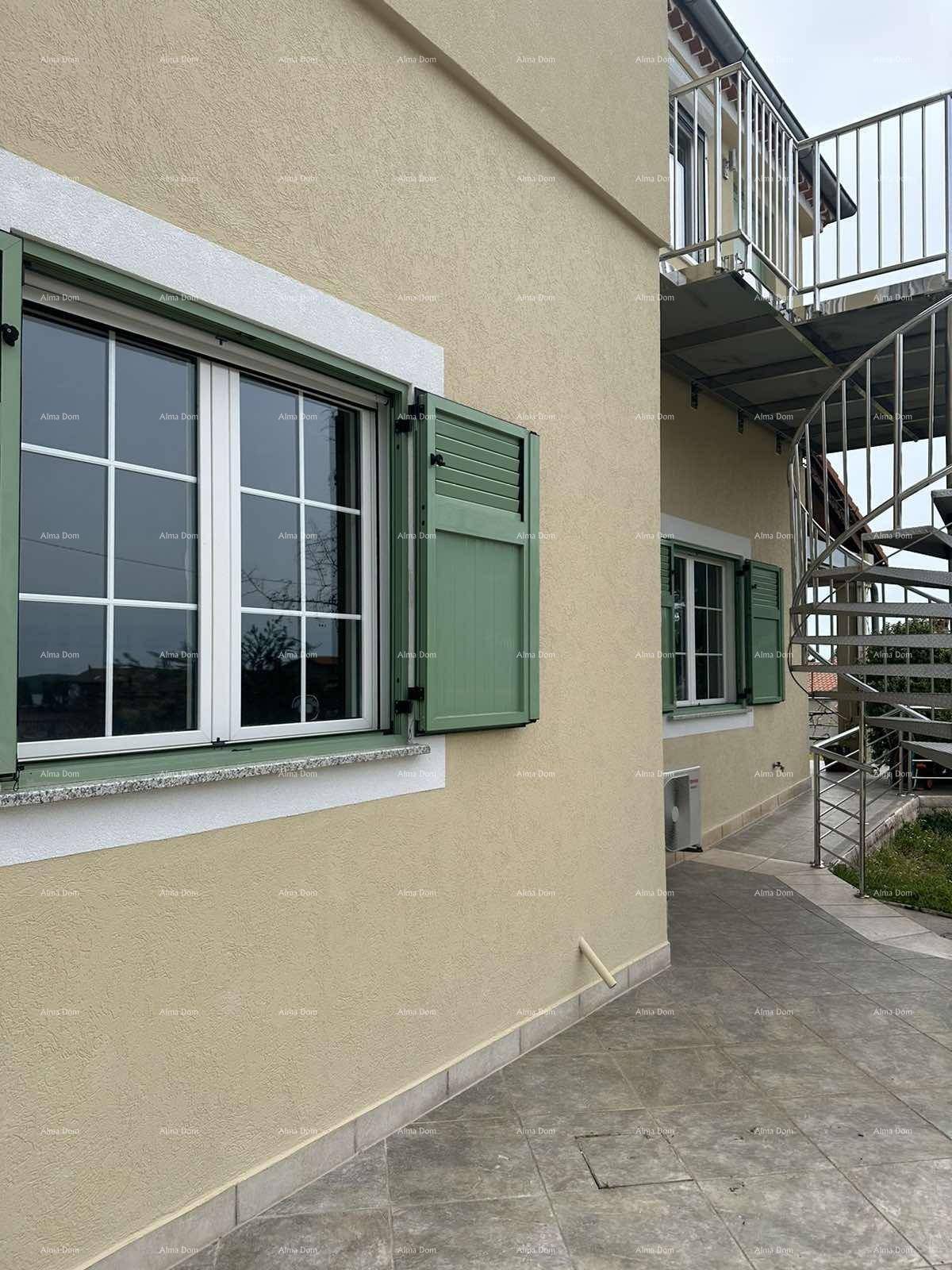 Gebäudefassade mit grünen Fensterläden und einer Außentreppe aus Metall.