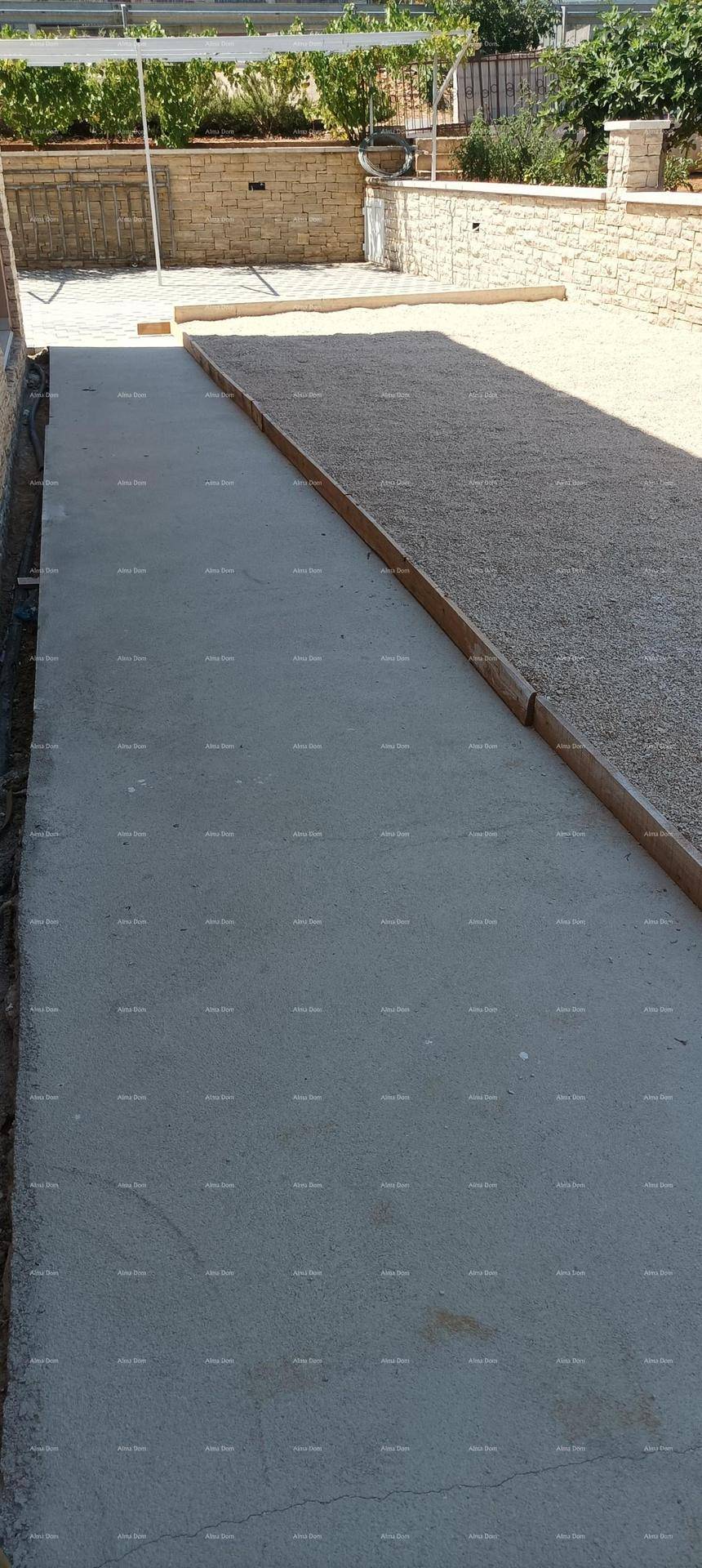 Außenbereich mit einem Kiesweg und einem angrenzenden Betonstreifen, umgeben von einer Steinmauer.